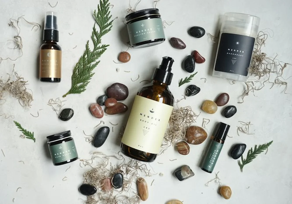 Overhead flat lay of a minimal skincare routine: frosted bottles, cotton pads and green leaves on pale mint linen